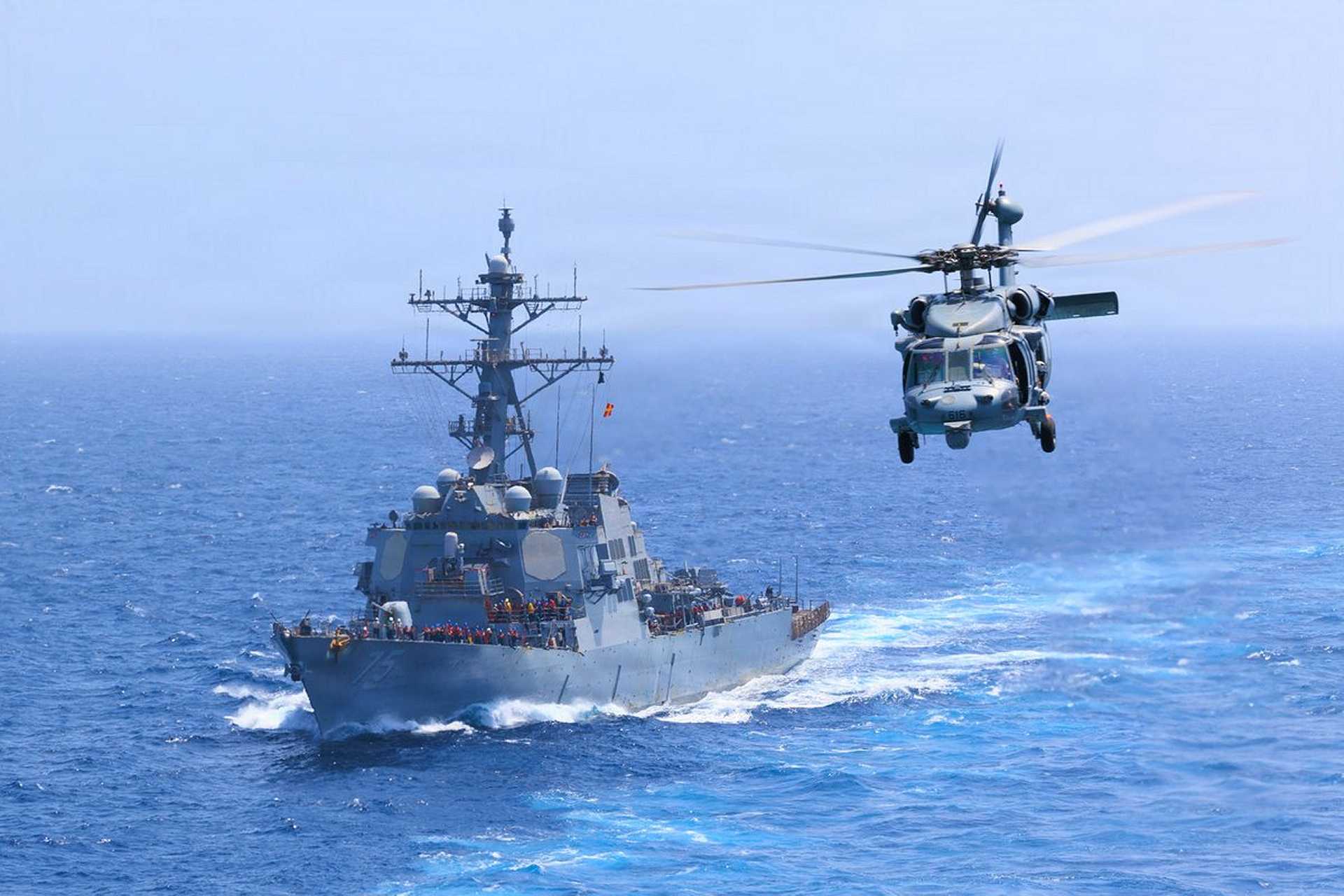 U.S. Navy USS Donald Cook (DDG 75) transits the Arabian Sea alongside an MH-60S Seahawk as U.S. forces intensify maritime interdiction operations against Iran, with CENTCOM reporting five commercial vessels diverted and one disabled as of July 18, 2026.