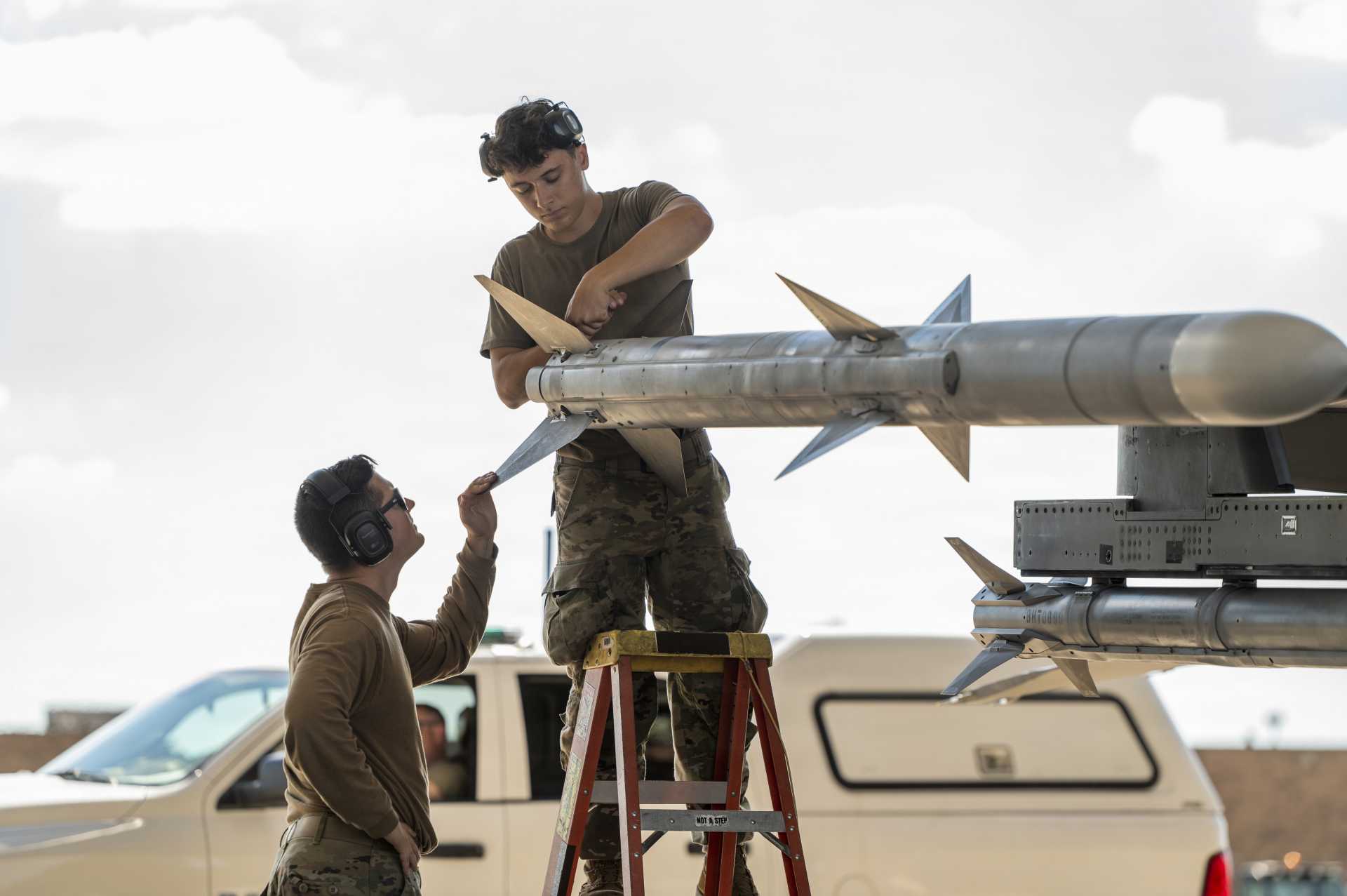U.S. Air Force Tech. Sgt. Jordon Gonzales and Airman 1st Class Lukas Pollock, aircraft armament systems specialists with the Ohio National Guard’s 180th Fighter Wing, prepare the fins of an AIM-120 AMRAAM air-to-air missile mounted on an F-16 Fighting Falcon before a training flight in Swanton, Ohio, on September 29, 2026. (Picture source: U.S. Department of War/Defense)