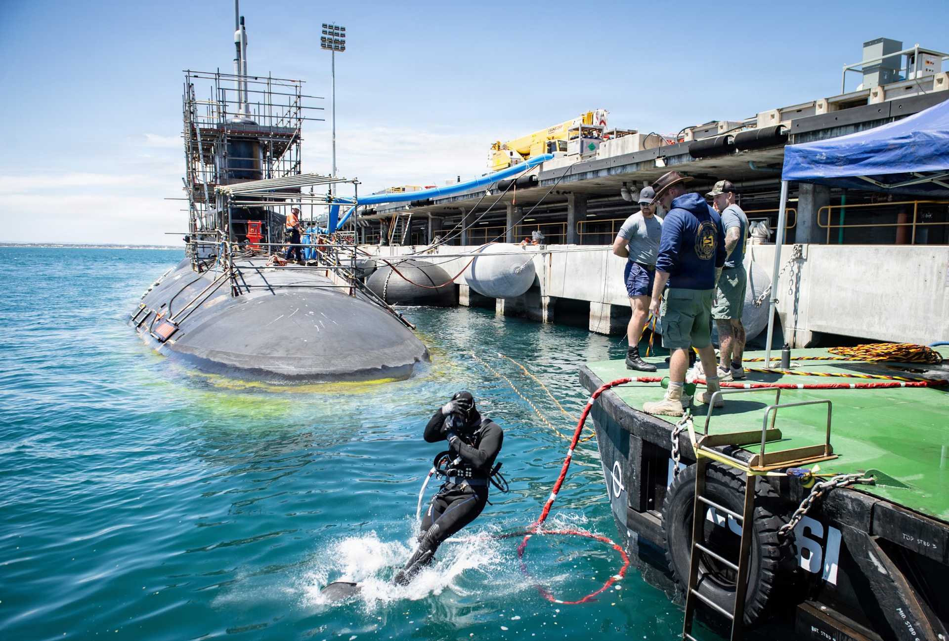 U.S. Navy sailors and Pearl Harbor Naval Shipyard civilian divers work with Royal Australian Navy Clearance Dive Team 4 beneath the hull of USS Vermont (SSN 792) during a planned submarine maintenance period, supporting AUKUS efforts to build Australian capacity for forward Virginia-class submarine sustainment.