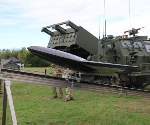 The jet-powered Nyan drone is displayed in front of a British Army M270A2 Multiple Launch Rocket System at DVD 2026, highlighting the growing integration of one-way attack drones with long-range artillery units to expand deep-strike options.