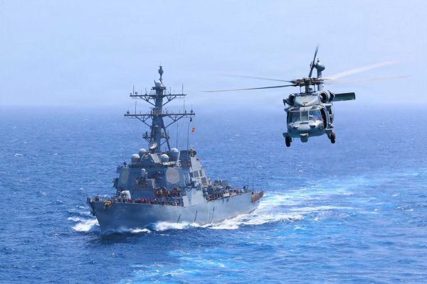 U.S. Navy USS Donald Cook (DDG 75) transits the Arabian Sea alongside an MH-60S Seahawk as U.S. forces intensify maritime interdiction operations against Iran, with CENTCOM reporting five commercial vessels diverted and one disabled as of July 18, 2026.